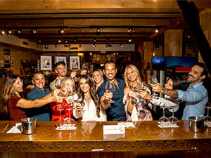 Group of people behind a bar toasting with wine glasses