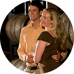 Happy couple posing in front of some wine barrels.