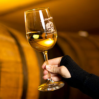 Hand holding up a glass of wine against a barrel background.